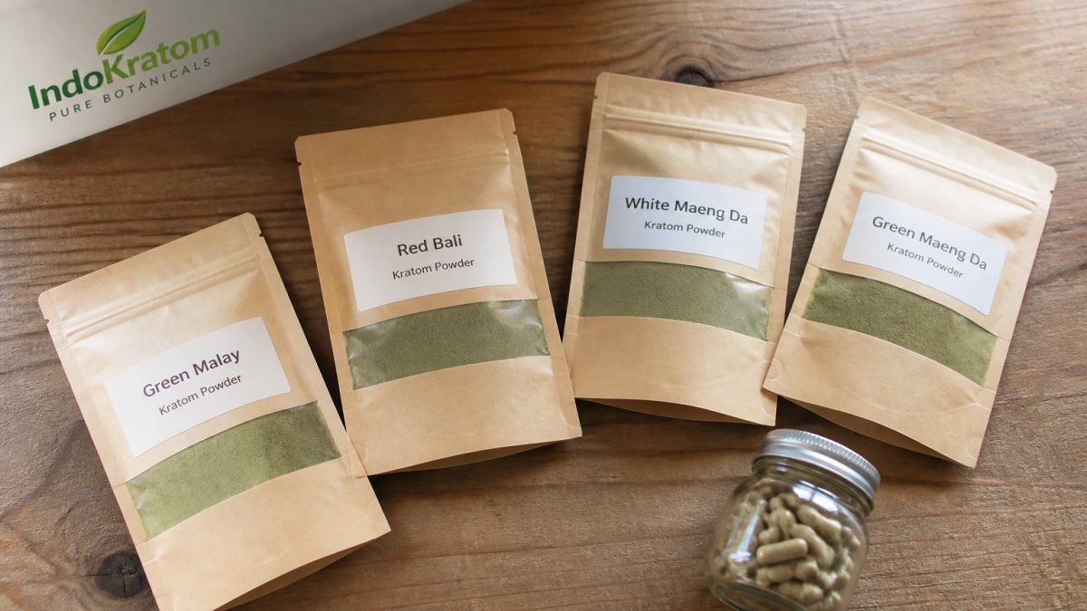 Overhead shot of labeled botanical powder pouches and a small glass jar of capsules arranged on a clean wooden table in natural light